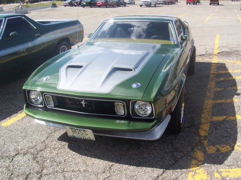 1973 Ford Mustang - A green Mustang with a silver hood and racing stripes is parked in a lot next to another vehicle.
