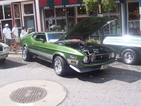 1973 Ford Mustang - A green 1971 Ford Mustang is displayed with its hood open, parked on a street next to another vehicle.