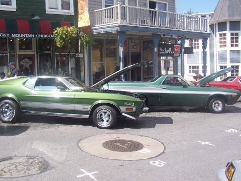 1973 Ford Mustang - A green 1971 Ford Mustang Mach 1 is parked on the street with its hood open, next to another vehicle.