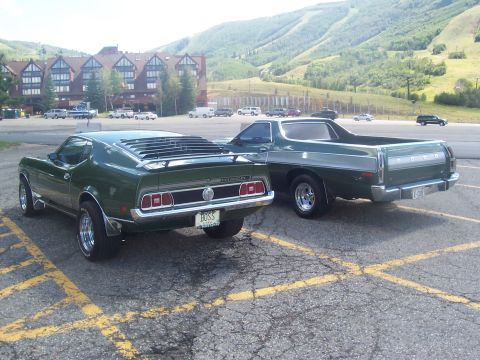 1973 Ford Mustang - A green 1971 Ford Mustang Mach 1 is parked next to a green Ford Ranchero in a parking lot with a lodge and mountains in the background.