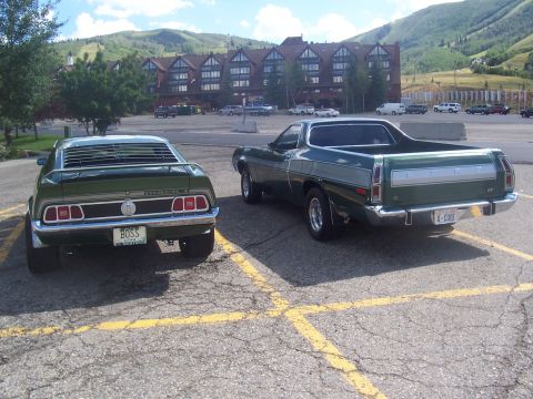 1973 Ford Mustang - Two green Ford vehicles, a 1973 Mustang and a Ford Ranchero, are parked in a lot with a lodge and mountains in the background.
