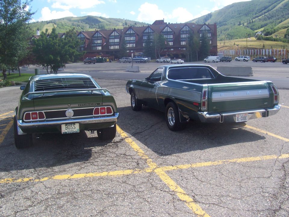 Rear view of green 1973 Ford Mustang with louvers and 'BOSS' plate, parked next to a Ford Ranchero