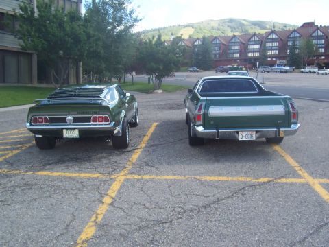1973 Ford Mustang - Two green Ford vehicles, a Mustang and a Ranchero, are parked in a lot with buildings and mountains in the background.