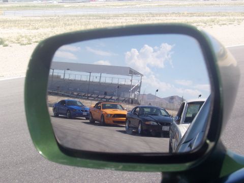 1973 Ford Mustang - A trio of Mustangs are seen on a race track, reflected in a side mirror.