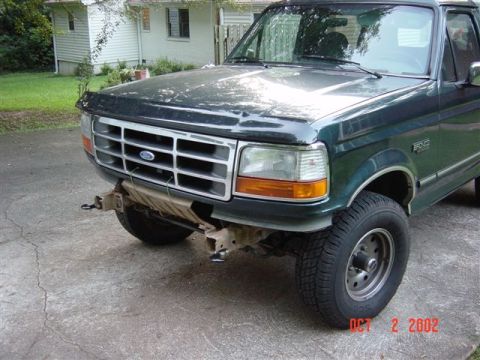 1995 Ford Bronco - Front view of a dark green Ford F-Series truck, showing damage to the bumper and lower front fascia.