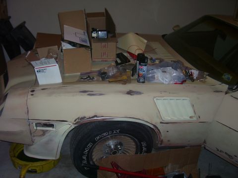 1979 Chevrolet Camaro - A 1979 Chevrolet Camaro is partially visible, covered in parts and boxes, with its hood and fender showing signs of repair.