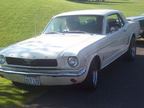 1973 Ford Mustang - White 1965 Ford Mustang coupe with chrome bumper and grille. Driver visible inside.
