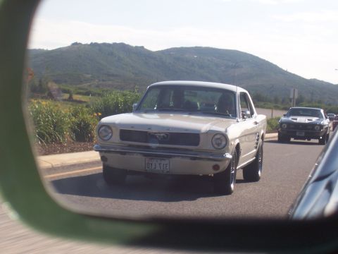 1973 Ford Mustang - A classic Mustang drives down the road, reflected in a side mirror, with another car following.