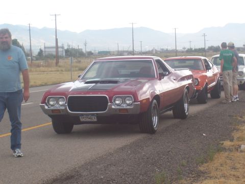 1973 Ford Mustang - A line of classic cars, including a red 1972 Ford Gran Torino Sport, are parked on the side of a road.