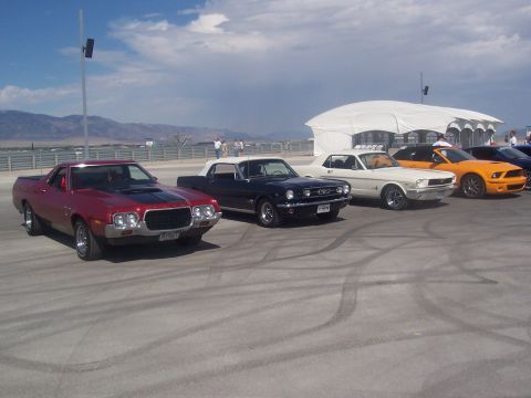 1973 Ford Mustang - A lineup of vehicles, ranging from classic to modern, are parked outdoors under a bright sky.