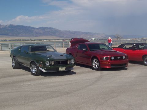 1973 Ford Mustang - A green 1971 muscle car is parked next to a red Ford Mustang, with mountains in the background.