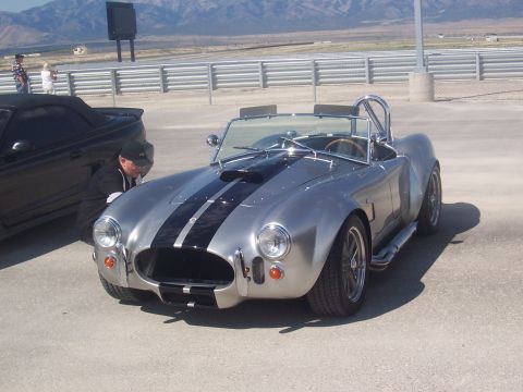 1973 Ford Mustang - A silver Shelby Cobra replica is parked next to a black convertible at an outdoor event.