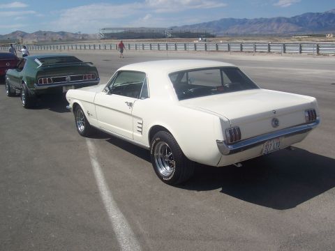 1973 Ford Mustang - A white coupe with a black vinyl roof is parked on a paved surface, with another green car behind it.