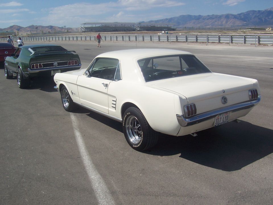 White coupe with a black vinyl roof, seen from the rear quarter angle on a paved surface