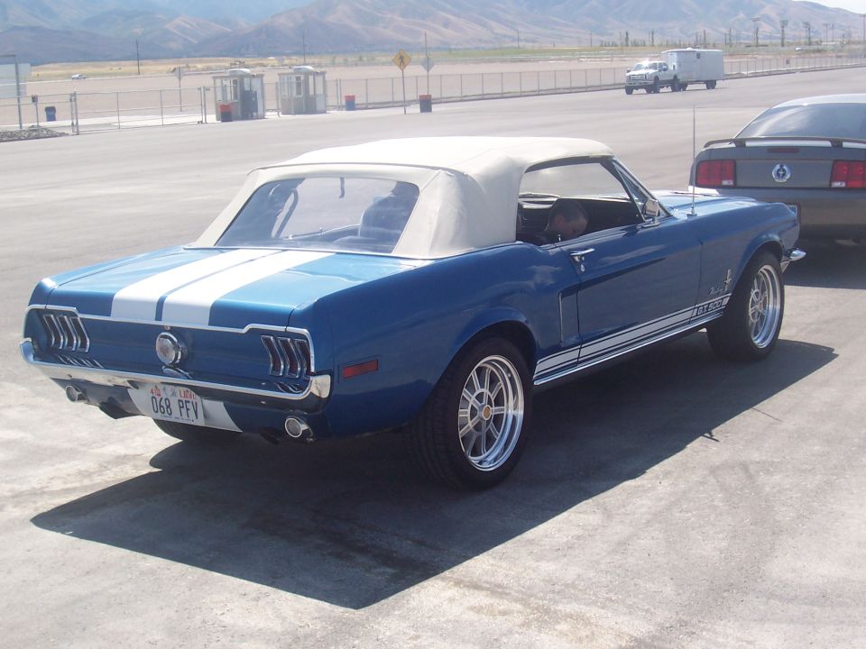 Blue convertible classic car with white racing stripes and a tan top parked next to another car