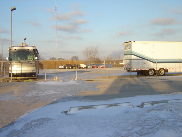 motorcoach parked next to a trailer in a snowy lot with other cars in background