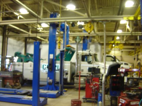 1992 Ford Bronco - A white tow truck is parked inside a garage with multiple vehicle lifts and equipment.