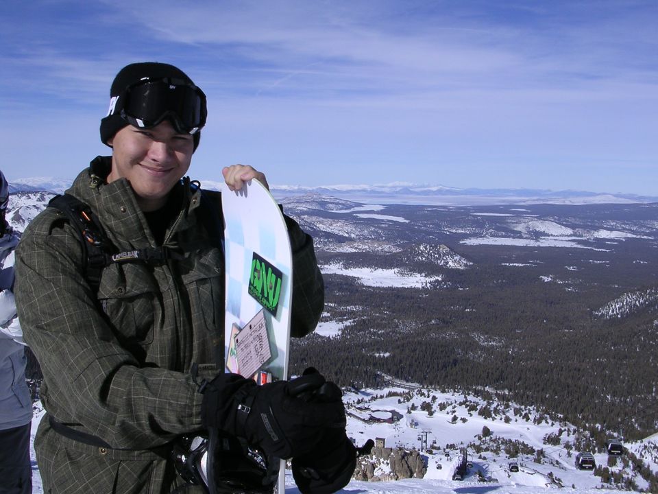 Guy holding snowboard on mountain with snowy landscape and blue sky