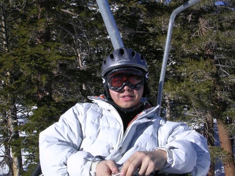 1983 Ferrari Enzo - A person wearing a helmet and goggles rides a ski lift through a snowy, wooded area.