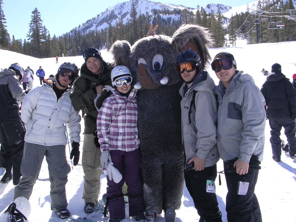 Group of friends in ski clothes posing with an elephant mascot on a snowy mountain