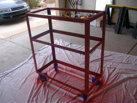 1995 Ford Bronco - A red metal cart with blue wheels sits on a drop cloth, with spray paint on the concrete floor.