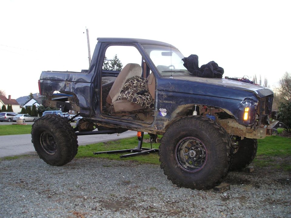 Blue pickup truck with removed doors and body panels, lifted suspension, and large off-road tires