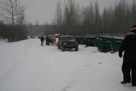 2003 Jeep TJ - Vehicles are parked on a snow-covered road near large dumpsters, with trees in the background.