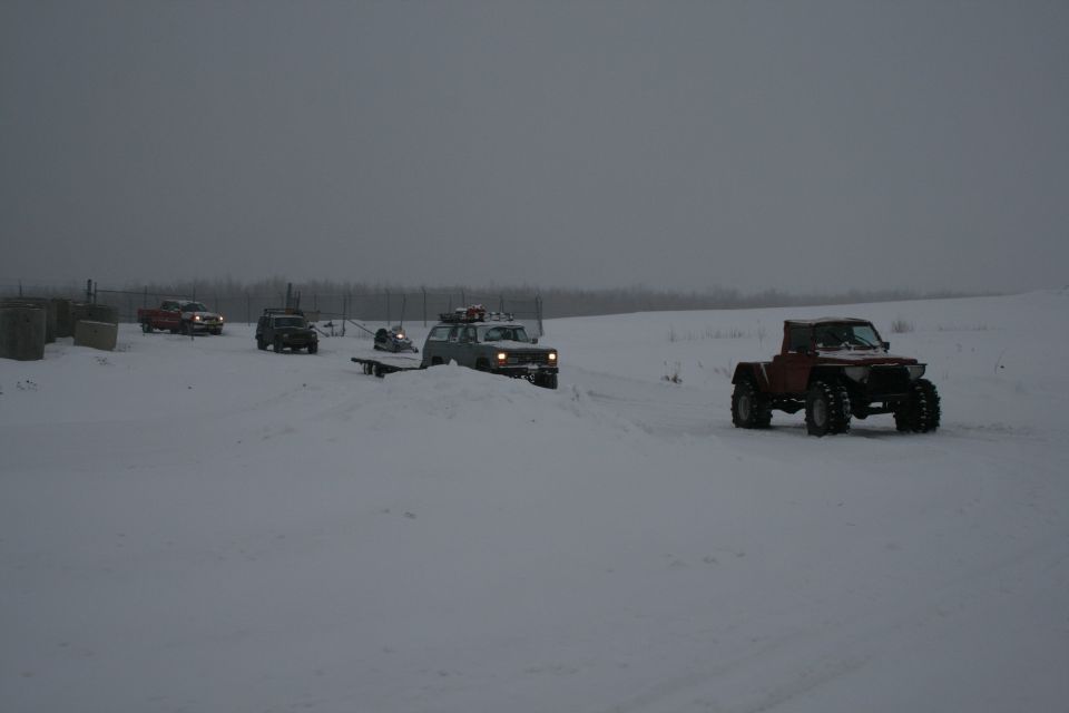 Several off-road vehicles driving in a snowy field under a cloudy sky