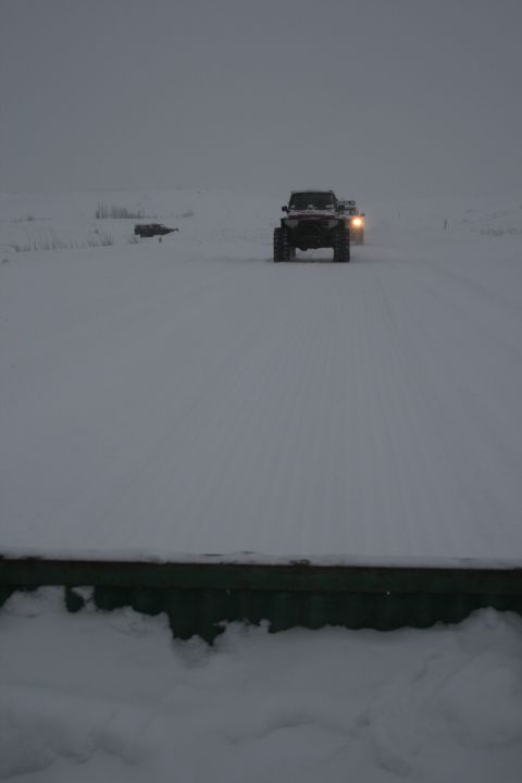 2003 Jeep TJ - Two SUVs drive down a snow-covered road with low visibility.