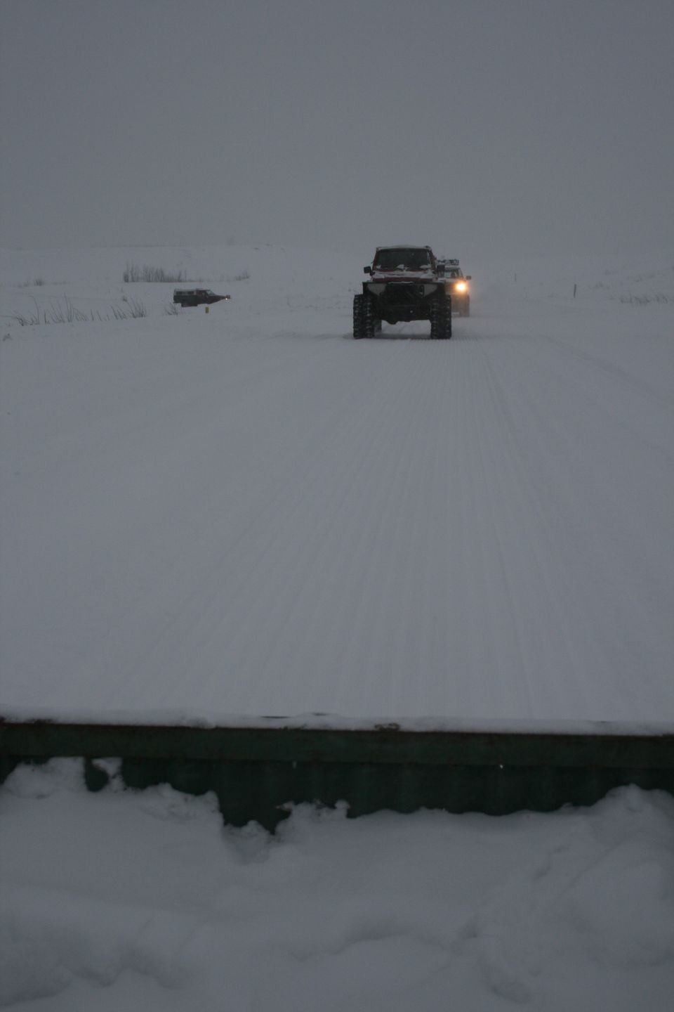 Two SUVs driving on a snowy road in overcast conditions