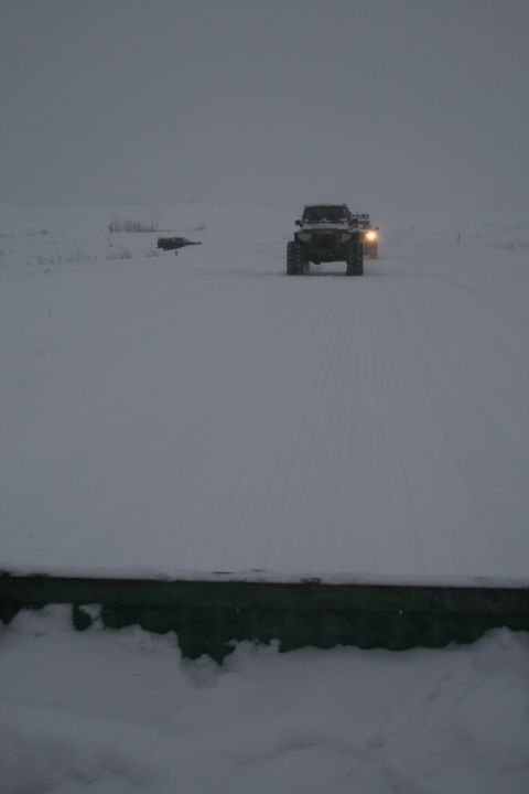 2003 Jeep TJ - A Jeep Wrangler drives through a snowy landscape with another vehicle following behind.