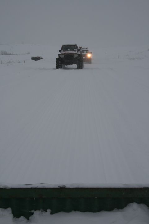 2003 Jeep TJ - Two off-road vehicles navigate a snowy landscape, their headlights cutting through the overcast sky.
