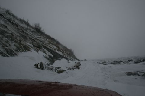 2003 Jeep TJ - A snowy scene with debris on the side of the road and two vehicles in the distance.