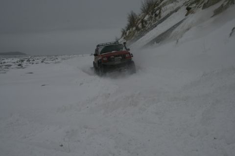 2003 Jeep TJ - A red 2003 Jeep TJ navigates a snowy terrain, kicking up snow as it drives.