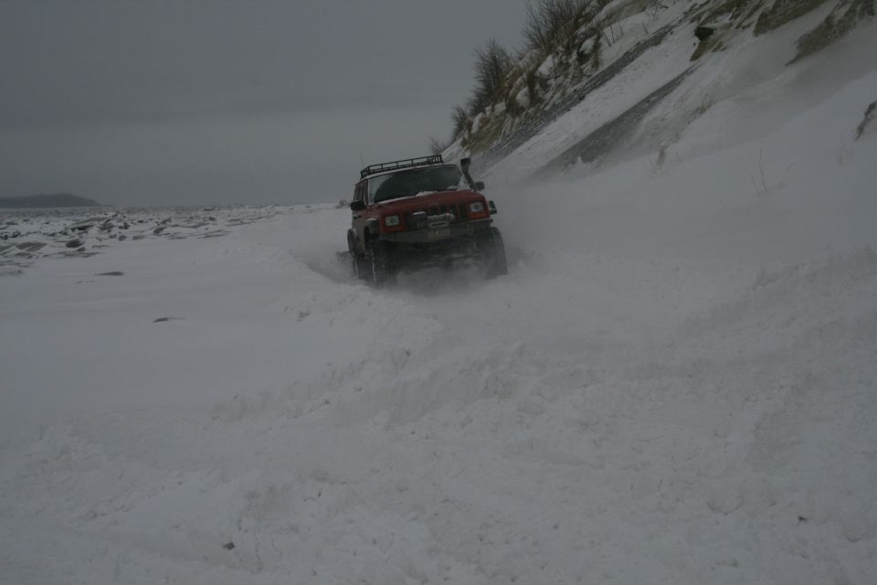 Red 2003 Jeep TJ driving through deep snow on a beach