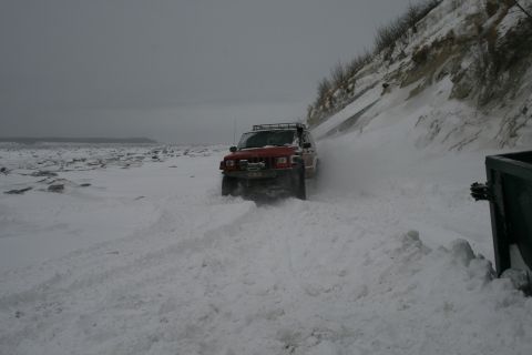 2003 Jeep TJ - A red Jeep Cherokee XJ navigates a snowy beach, kicking up snow as it drives towards the camera.