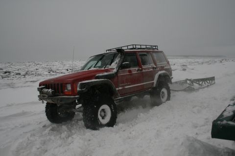 2003 Jeep TJ - A red Jeep Cherokee XJ navigates a snowy landscape, equipped with off-road modifications and towing a trailer.