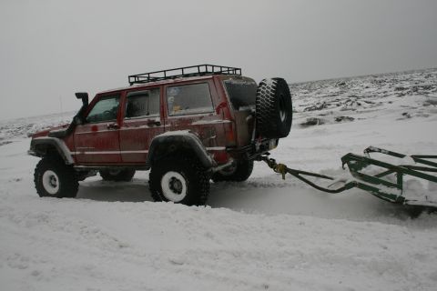 2003 Jeep TJ - A red Jeep Cherokee XJ is seen from the rear-three-quarter view, towing a sled through a snowy landscape.