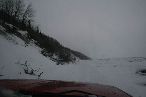 2003 Jeep TJ - View from inside a red vehicle driving through a snowy landscape with trees on a hill.