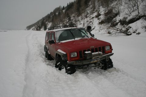 2003 Jeep TJ - Red Jeep Cherokee XJ navigates a snowy trail with a winch and roof rack.