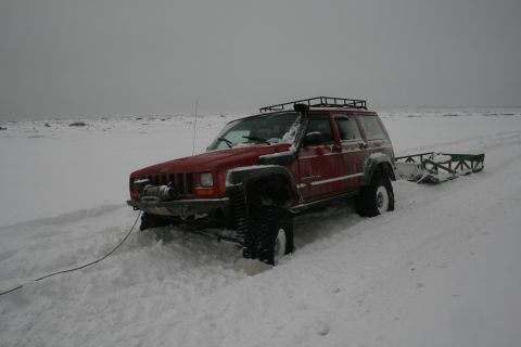 2003 Jeep TJ - A red Jeep Cherokee XJ is stuck in the snow while pulling a sled in a barren, overcast landscape.