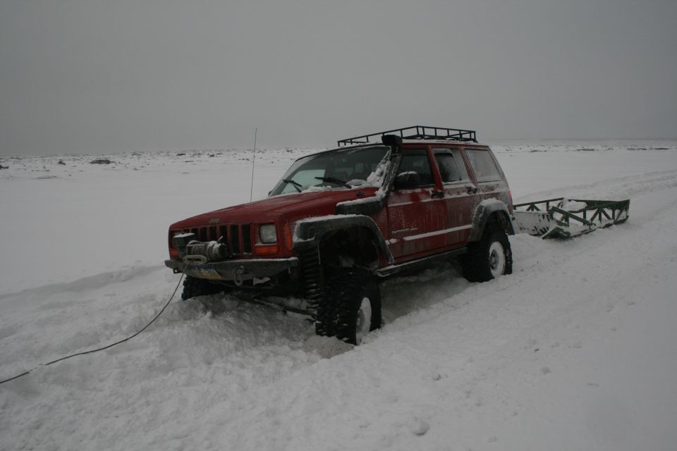 Red Jeep Cherokee XJ with snorkel and roof rack in snow, pulling a sled