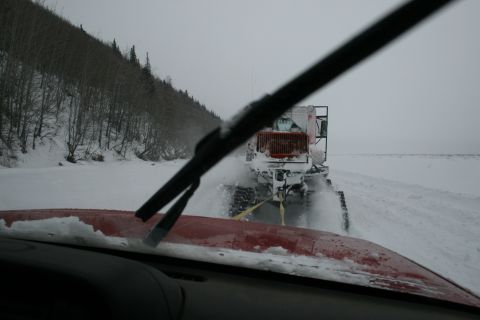2003 Jeep TJ - A red vehicle's hood, covered in snow, is seen from inside as it tows a white snowcat vehicle through a snowy, overcast landscape.