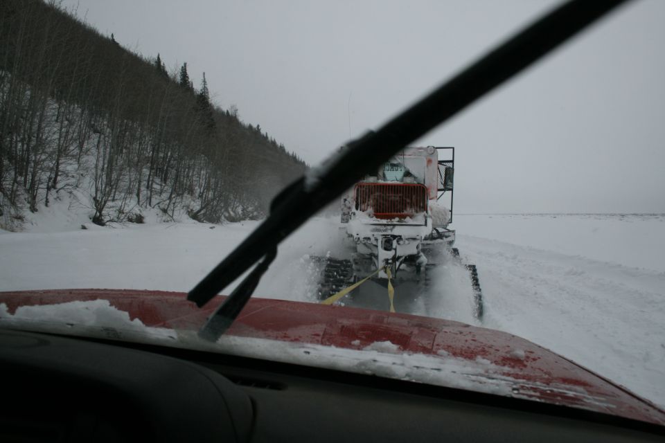 Red vehicle hood with snow, towing a white snowcat vehicle with orange grille in a snowy landscape