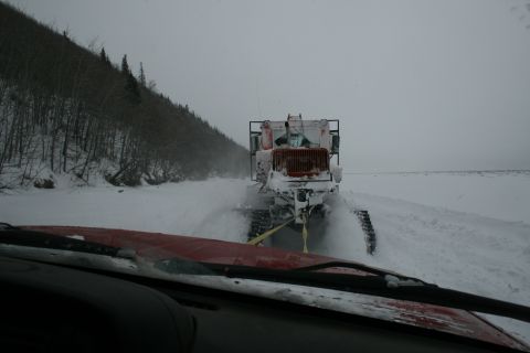 2003 Jeep TJ - A snowcat vehicle is seen from inside another vehicle, moving through a snowy landscape with trees on the left.