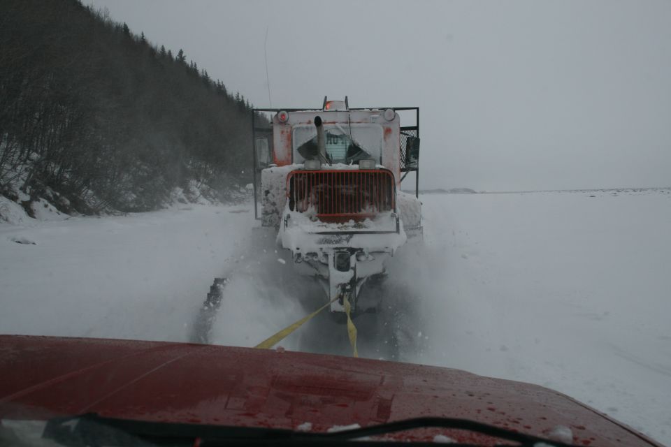 Front view of a snow plow truck being towed by another vehicle in a snowy landscape