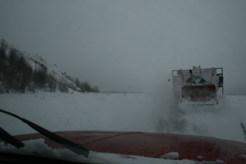 2003 Jeep TJ - A snowplow truck operates in a snowy, overcast environment, viewed from the perspective of another vehicle.