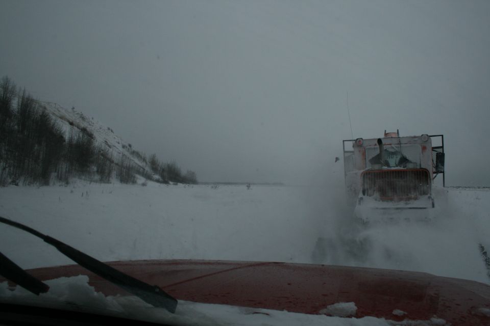 View from inside a vehicle looking at a snowplow truck clearing snow on a cloudy day