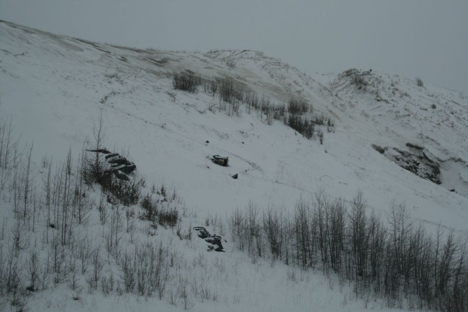 Snowy hillside with scattered debris and bare trees