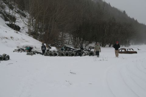 2003 Jeep TJ - Snowy scene with a rusted car body and stacks of tires, people are visible in the background.